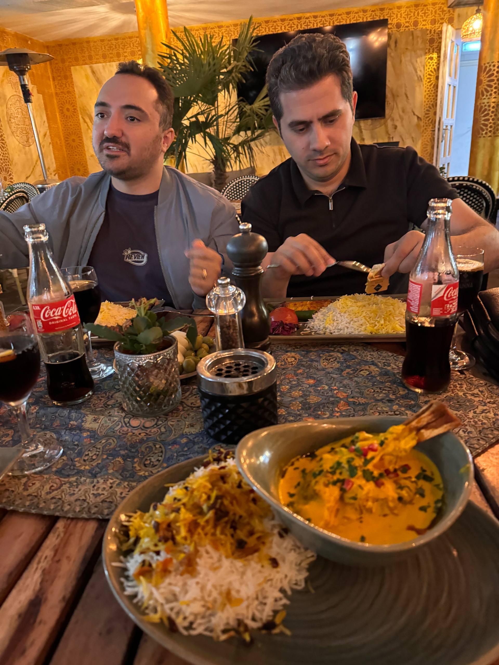 Mohammed and a friend eating Persian food at Hafez restaurant in Munich, with rice, stew, and Coca-Cola bottles on the table