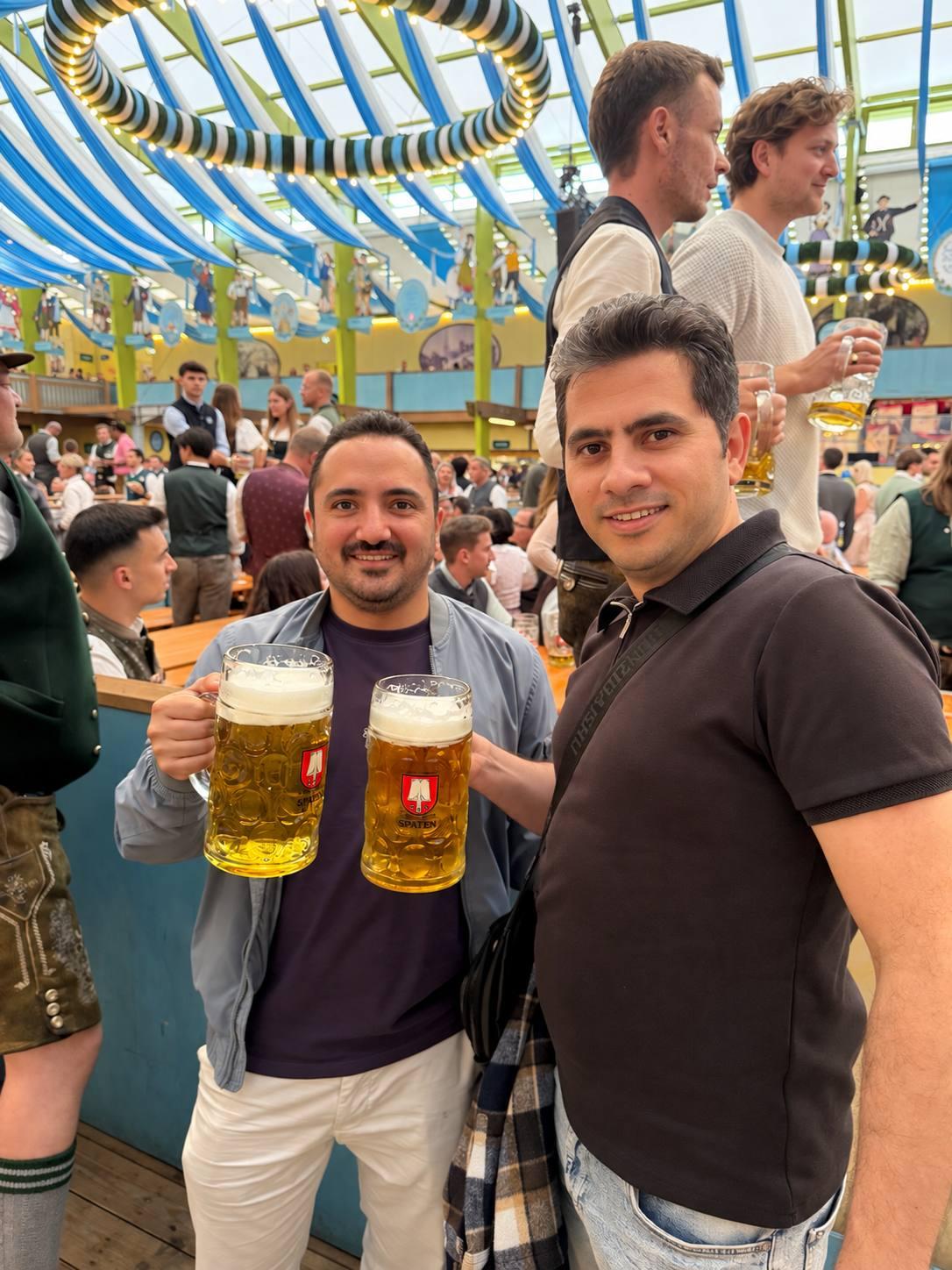 Mohammed and a friend holding one-liter beer mugs inside a crowded Oktoberfest beer tent