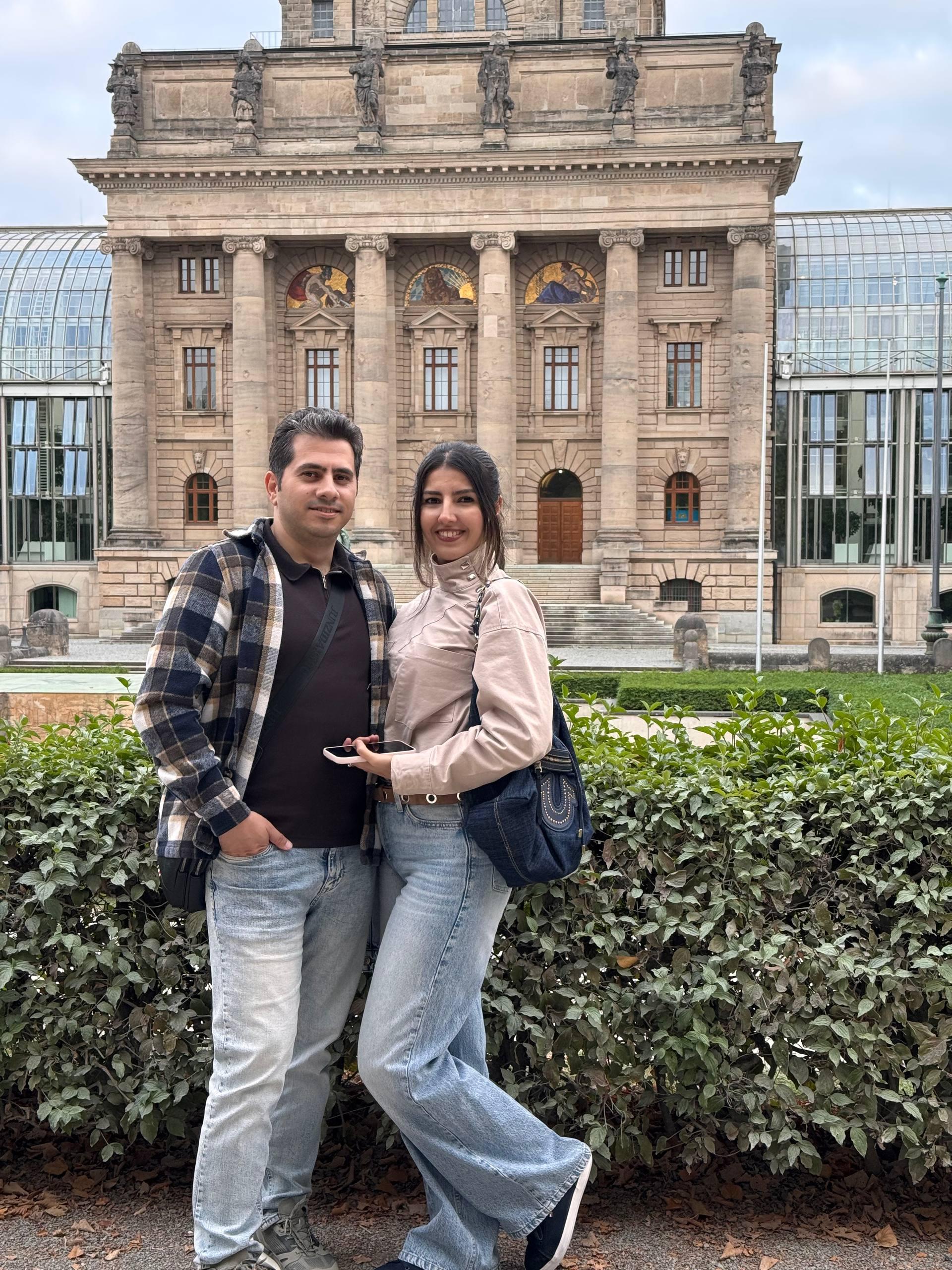Mohammed and his wife in front of the Bavarian State Chancellery building in Munich, with its glass wings visible on either side