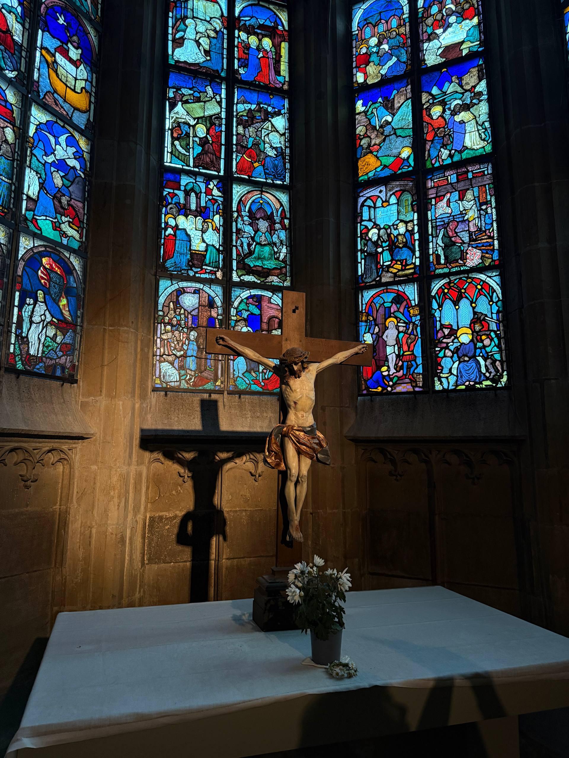 A wooden crucifix in front of colorful stained-glass windows at the altar of Ulm Minster