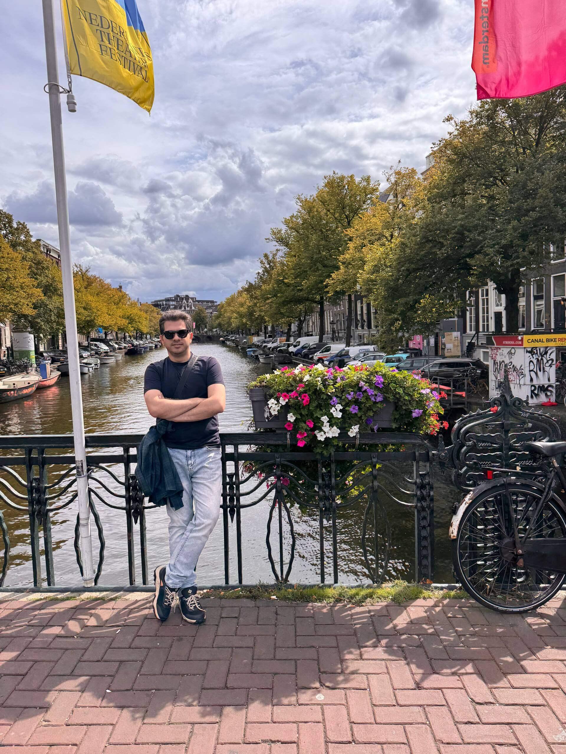 Mohammed standing on a bridge over an Amsterdam canal, with a bicycle and flower box beside him