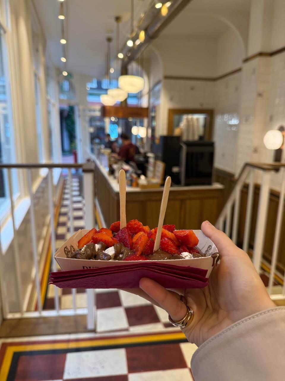 A waffle topped with strawberries and chocolate, held in hand, at Pat's in Amsterdam