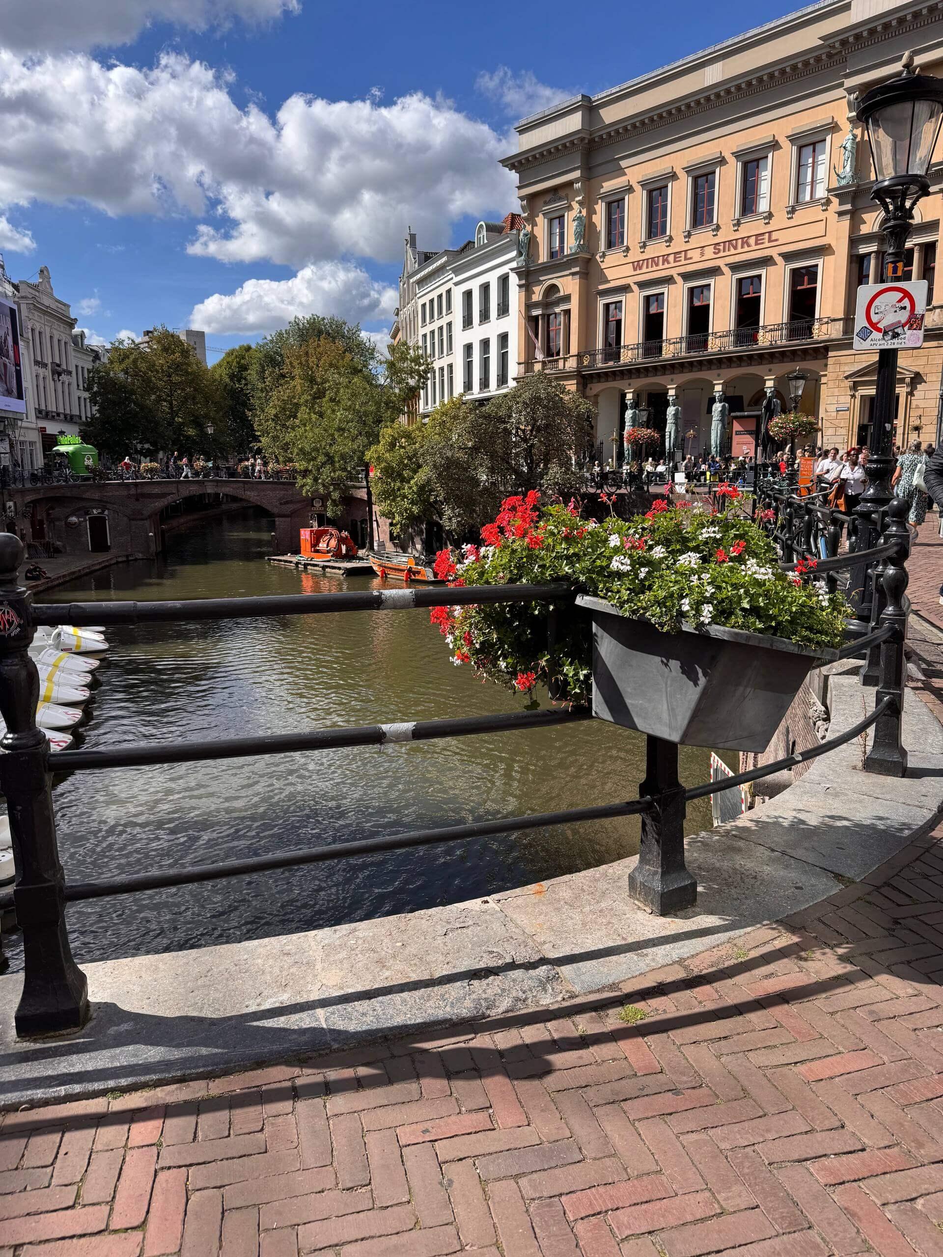 A canal in Utrecht lined with flower boxes, boats, and the historic Winkel van Sinkel building in the background