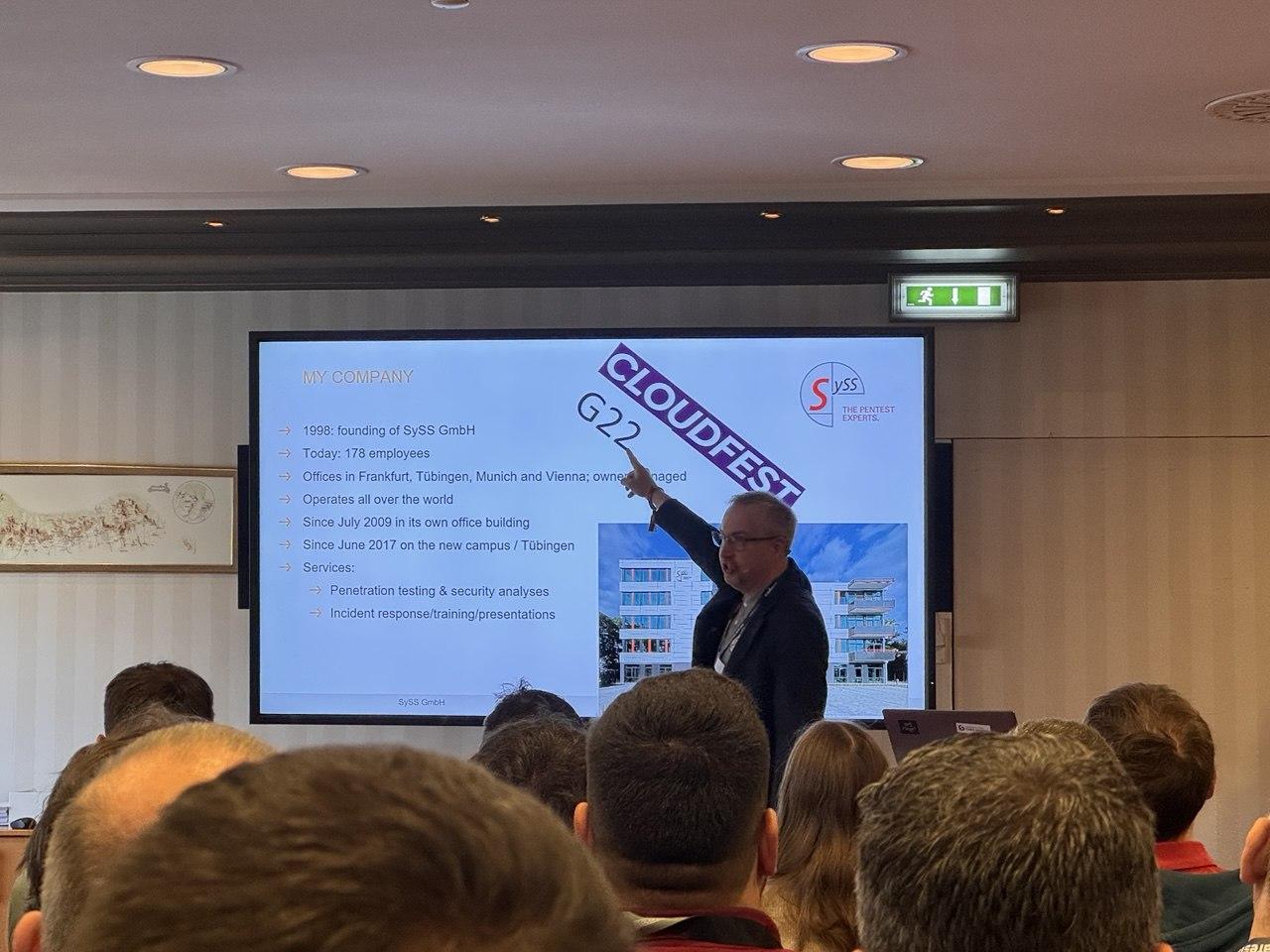 A speaker presenting on penetration testing, with a SySS GmbH slide behind him